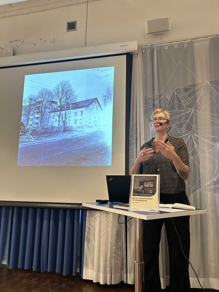En kvinna står framför en bild av ett gammalt hus.
