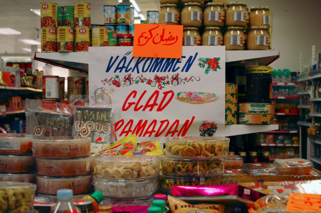 En skylt med texten välkommen glad ramadan står omringad av mat och sötsaker i en matbutik.