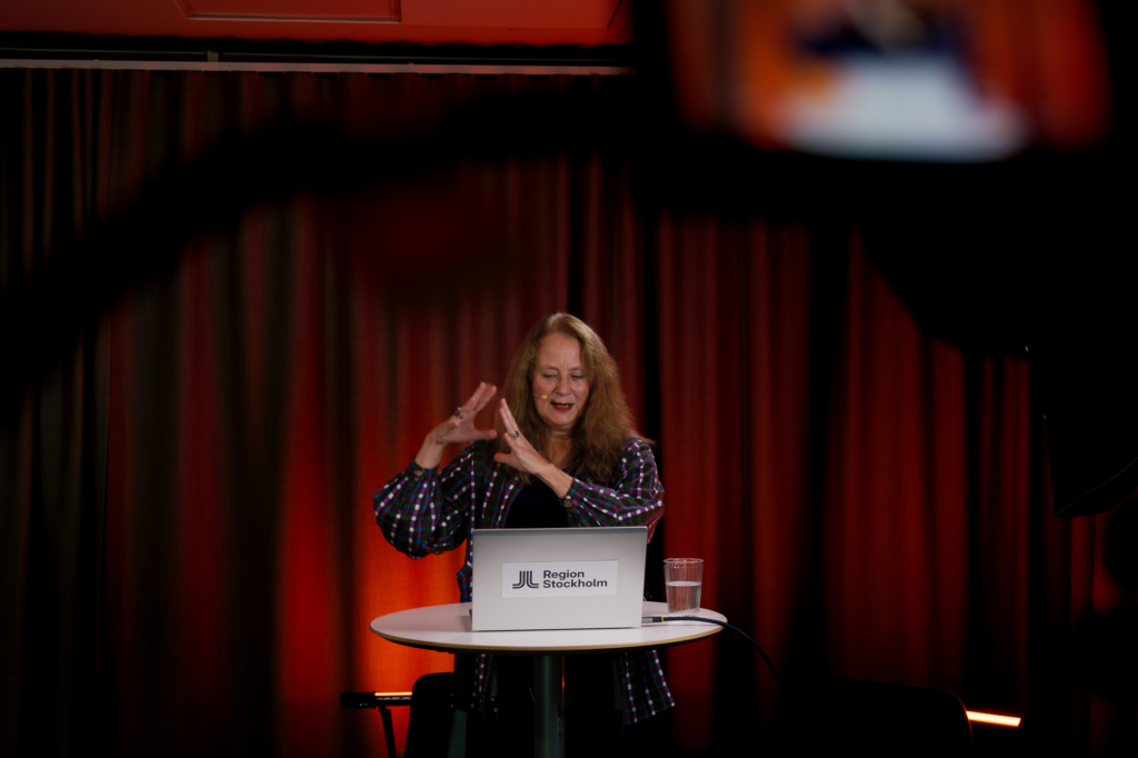 En kvinna står vid ett bord och pratar inför en kamera.
